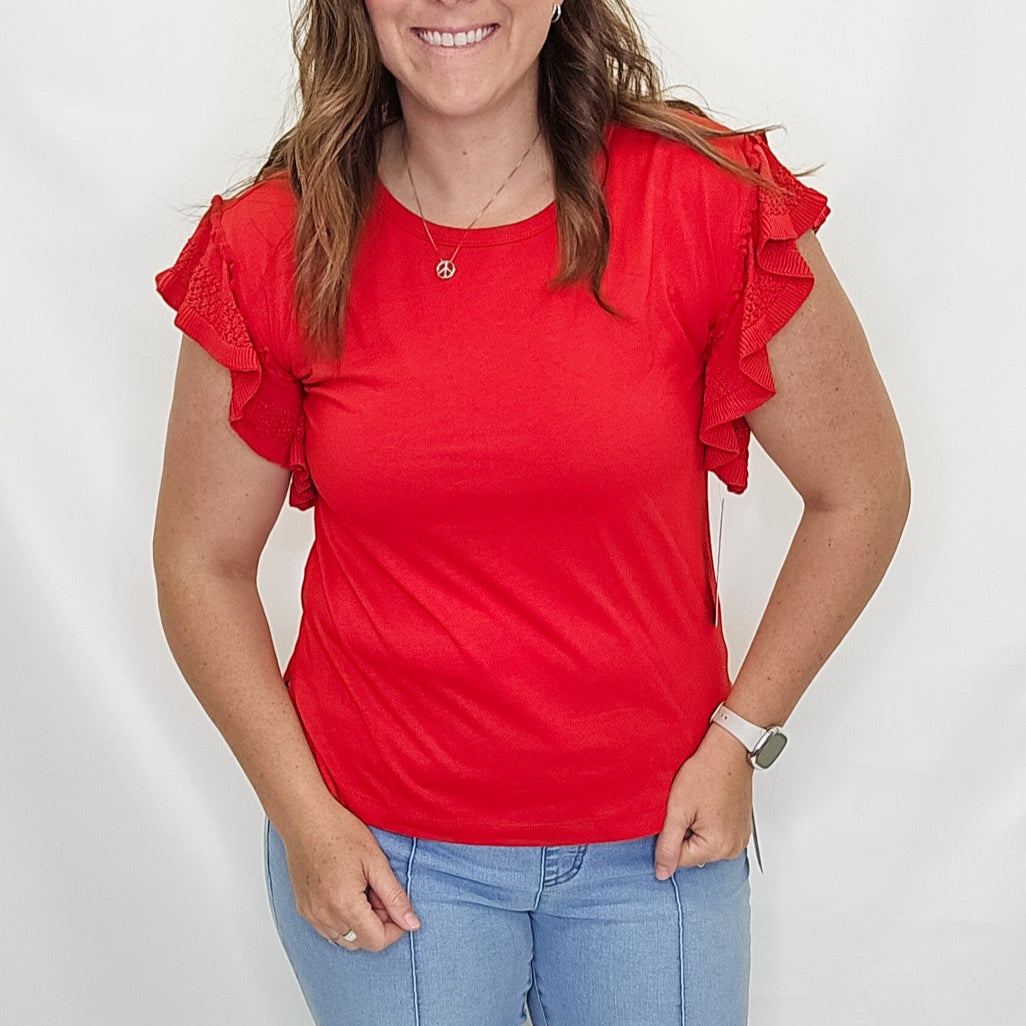 Woman wearing a red top with ruffled sleeves and blue jeans on a white background