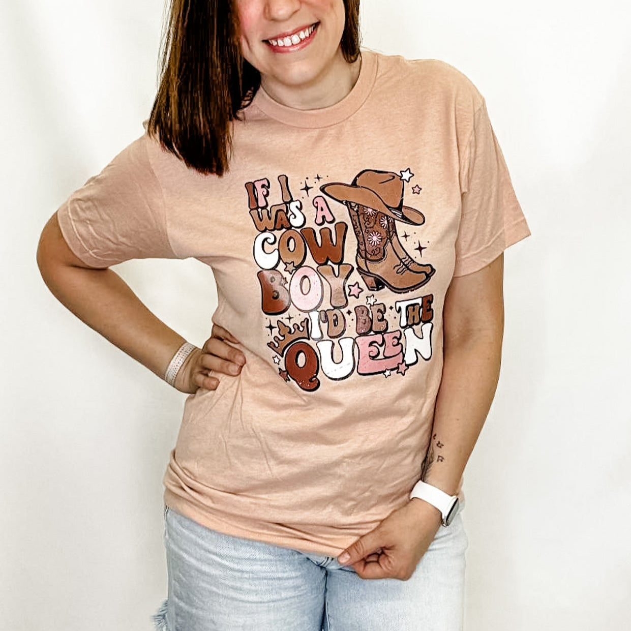 Woman wearing a beige t-shirt with a graphic design and text, standing against a white background