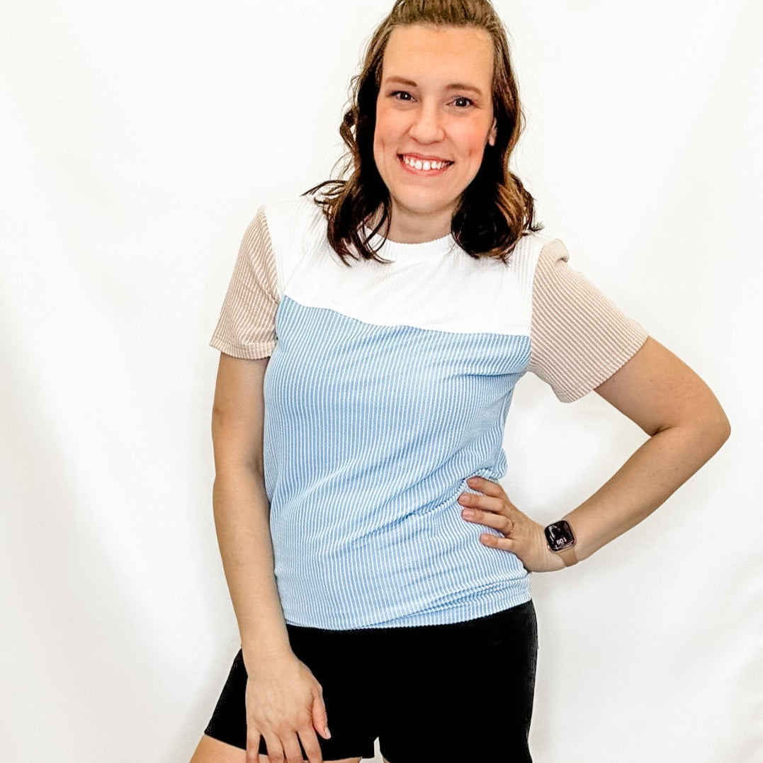 Woman wearing a light blue and beige top with black shorts on a white background